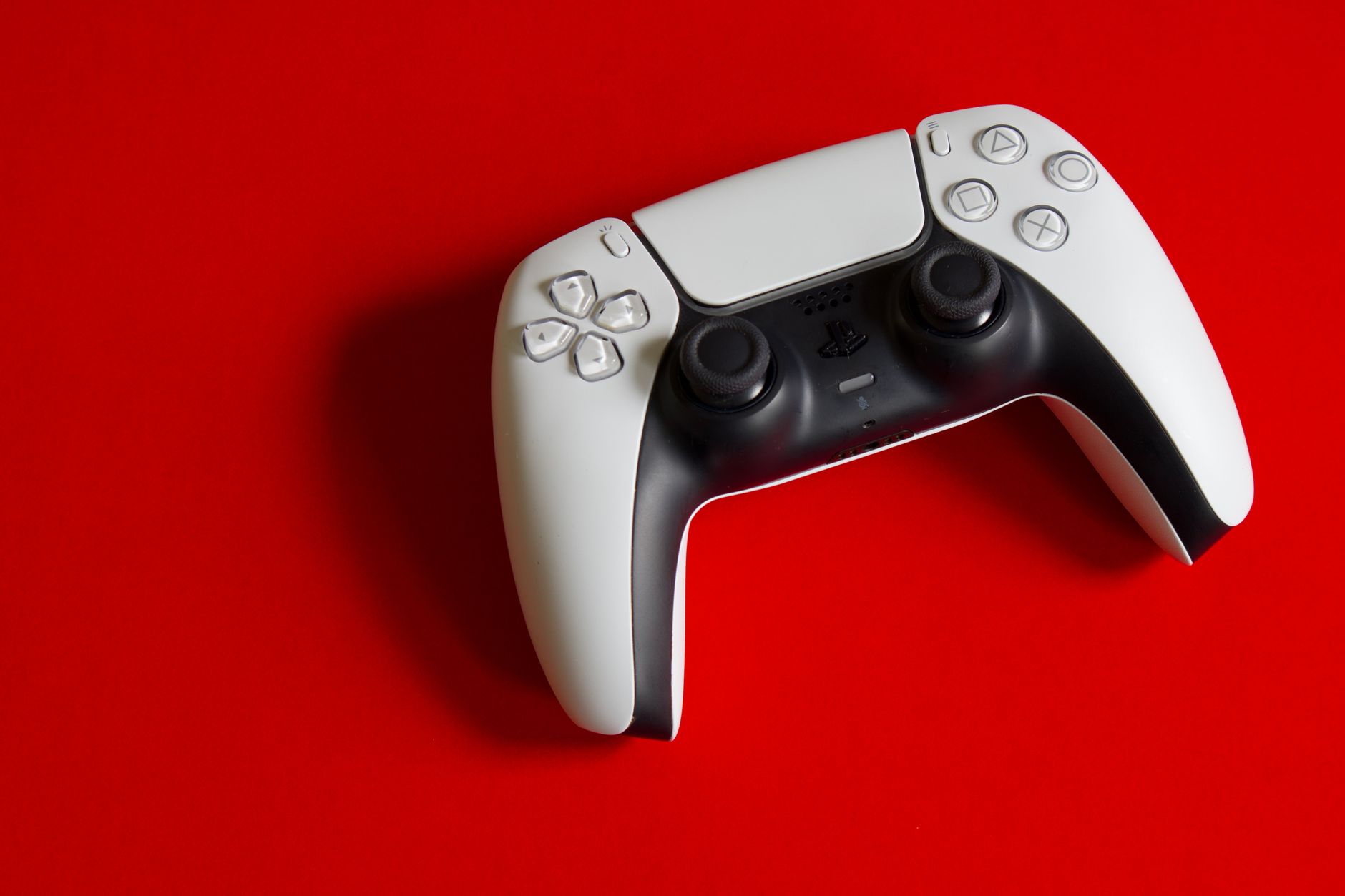 White DualSense controller for PlayStation 5 on a striking red backdrop, emphasizing modern gaming technology.