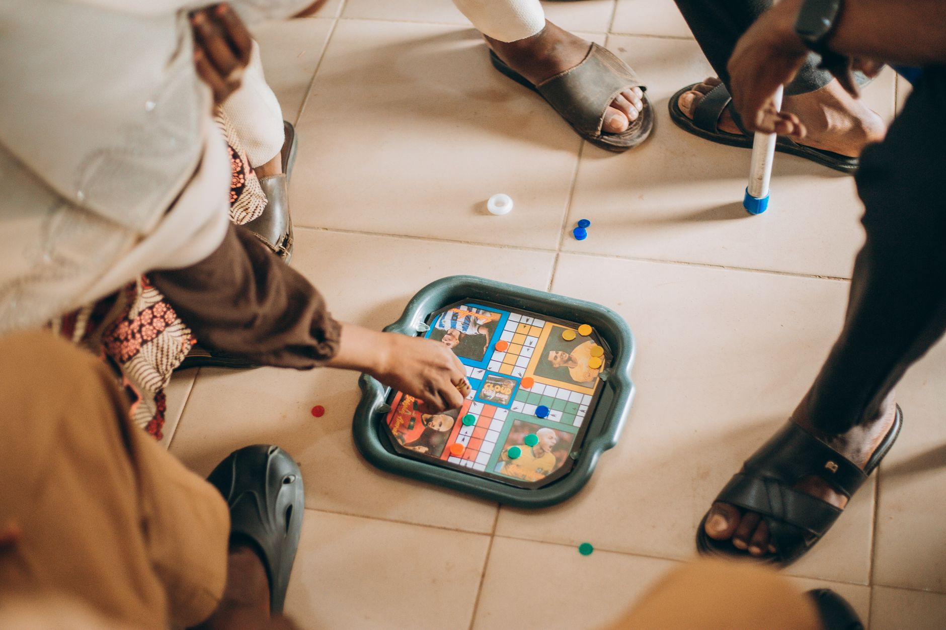 Group of children playing board game indoors on a tiled floor, focused on the game pieces.
