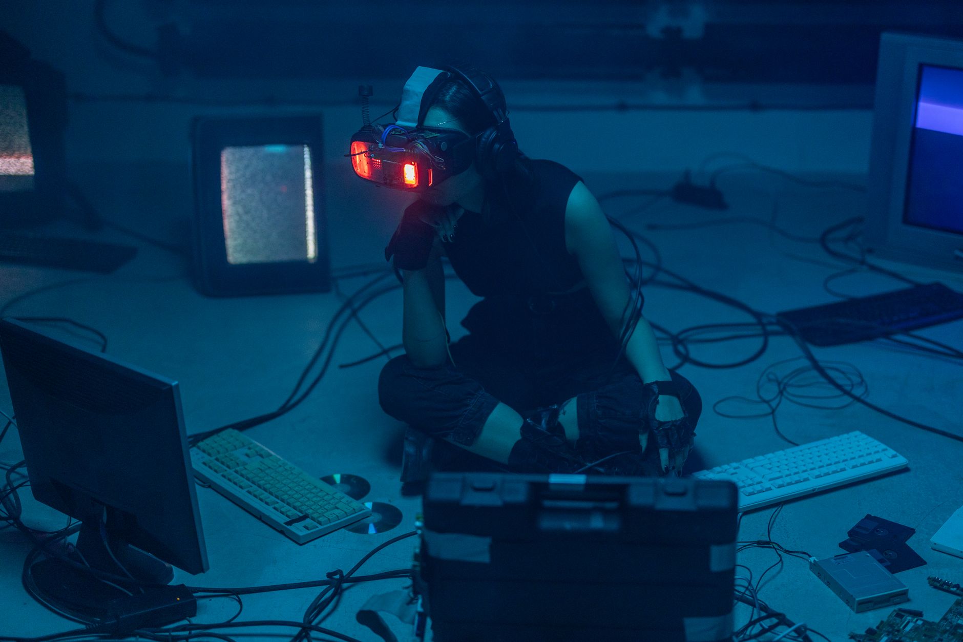A woman in a dark room wearing a VR headset surrounded by retro technology.
