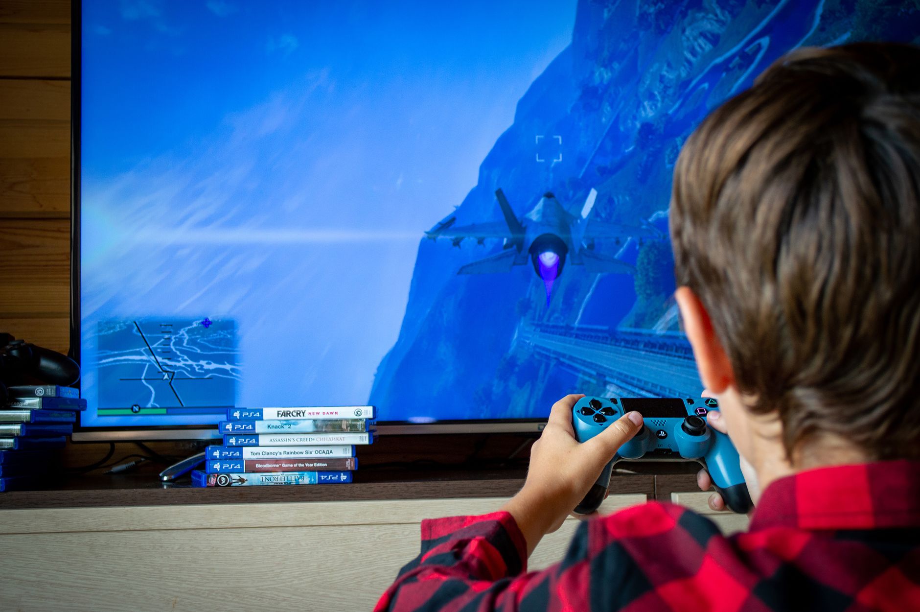 Young boy playing video game on TV with PS4 controller, enjoying leisure time indoors.