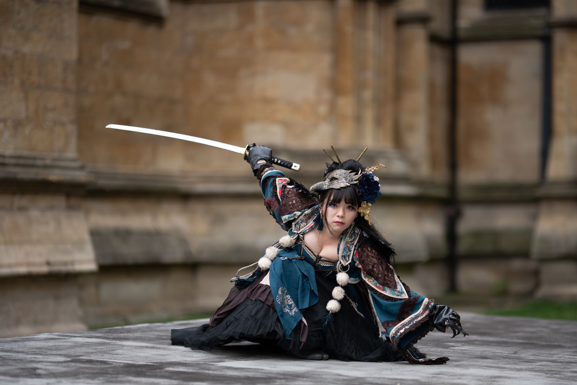 Female performer in traditional samurai costume poses with sword outdoors.
