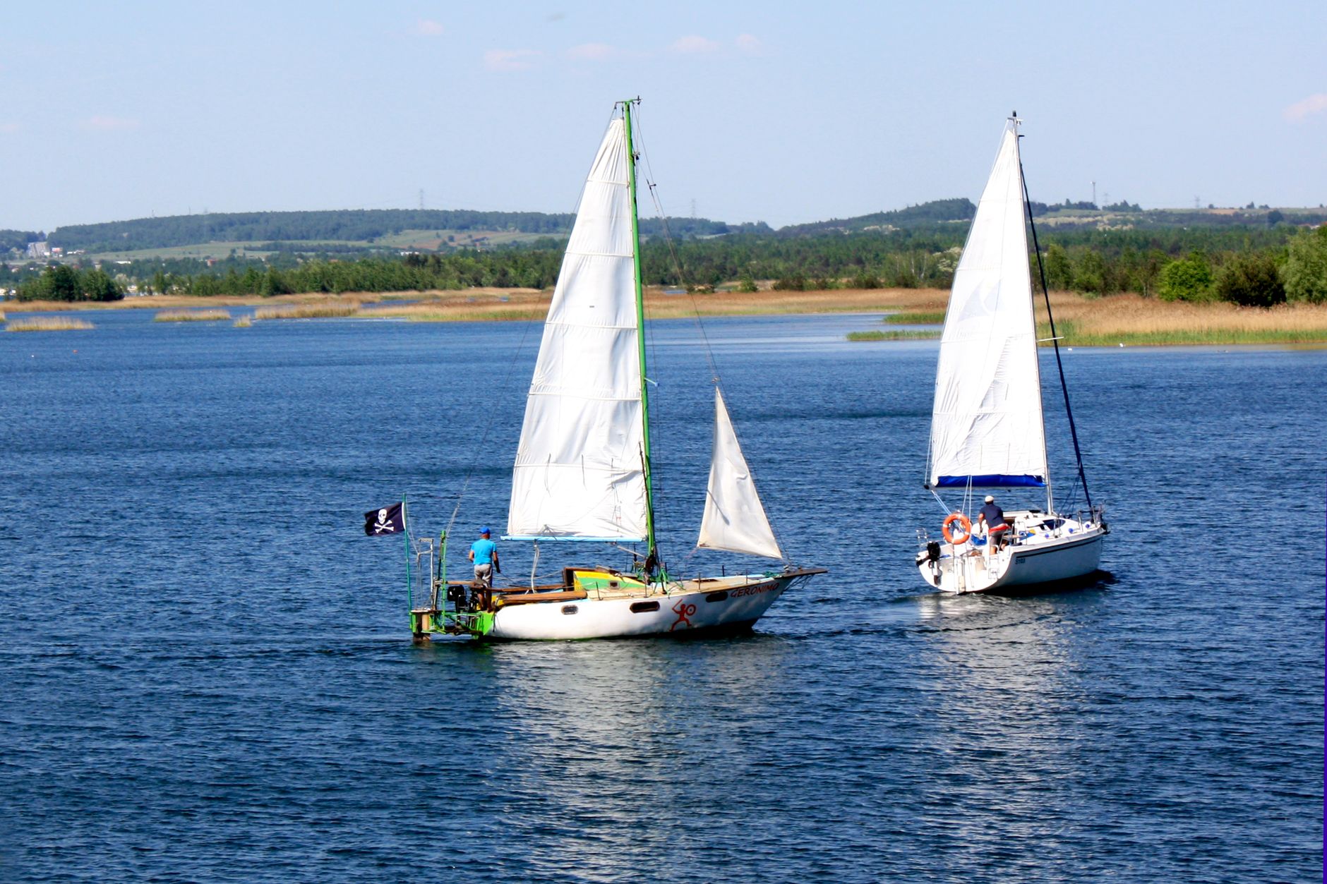 Two sailboats gracefully navigating a tranquil lake under clear blue skies.