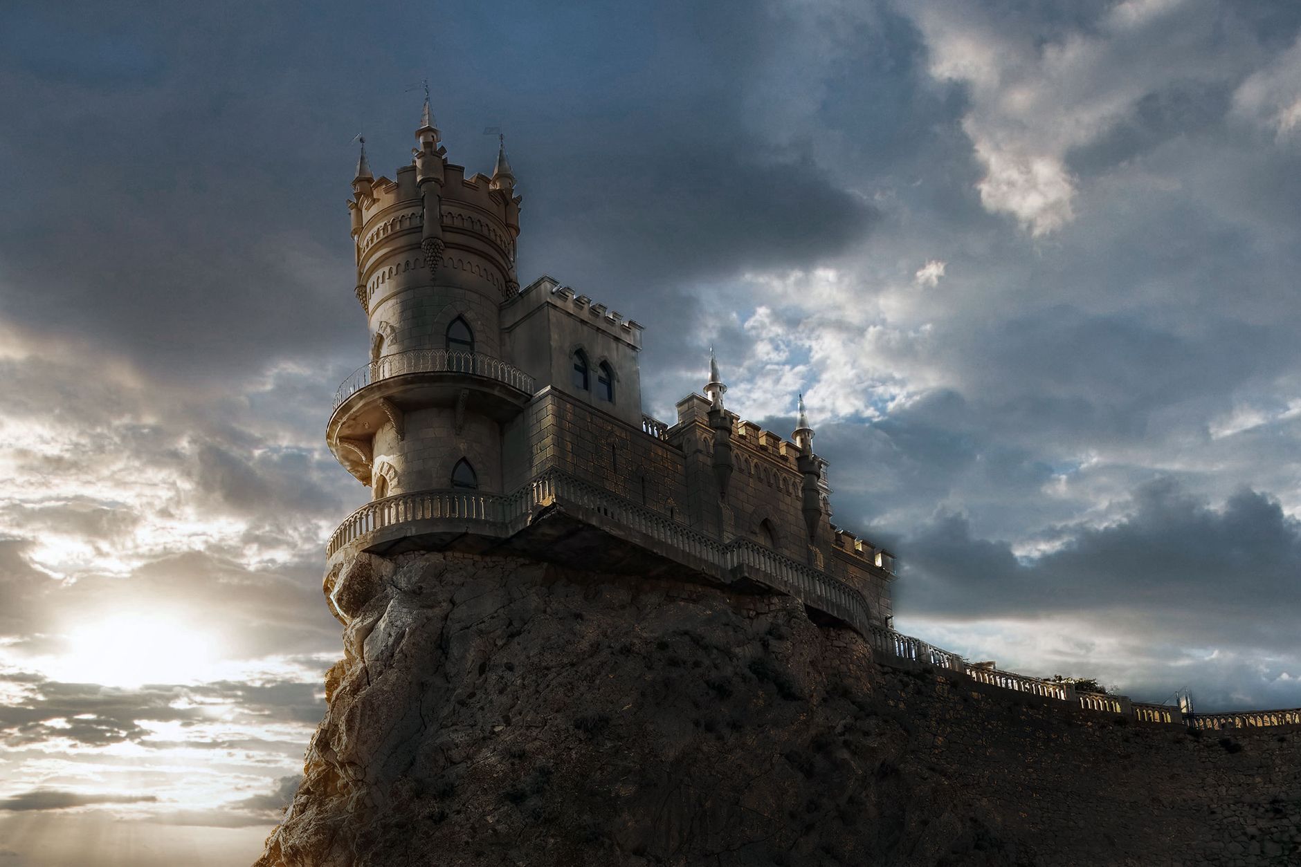 From below of ancient stone castle with fence located on top of mountain against cloudy sky in evening time in nature