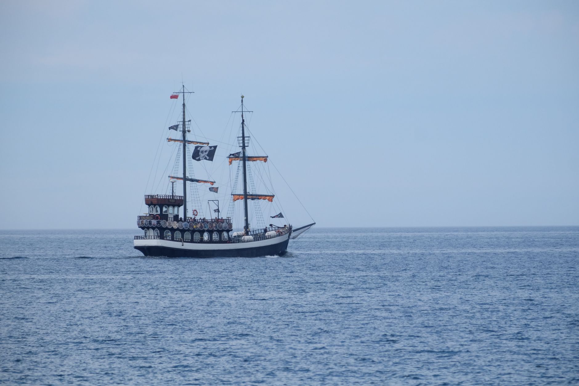 A vintage pirate ship with sails unfolds on calm ocean waters under a clear sky.