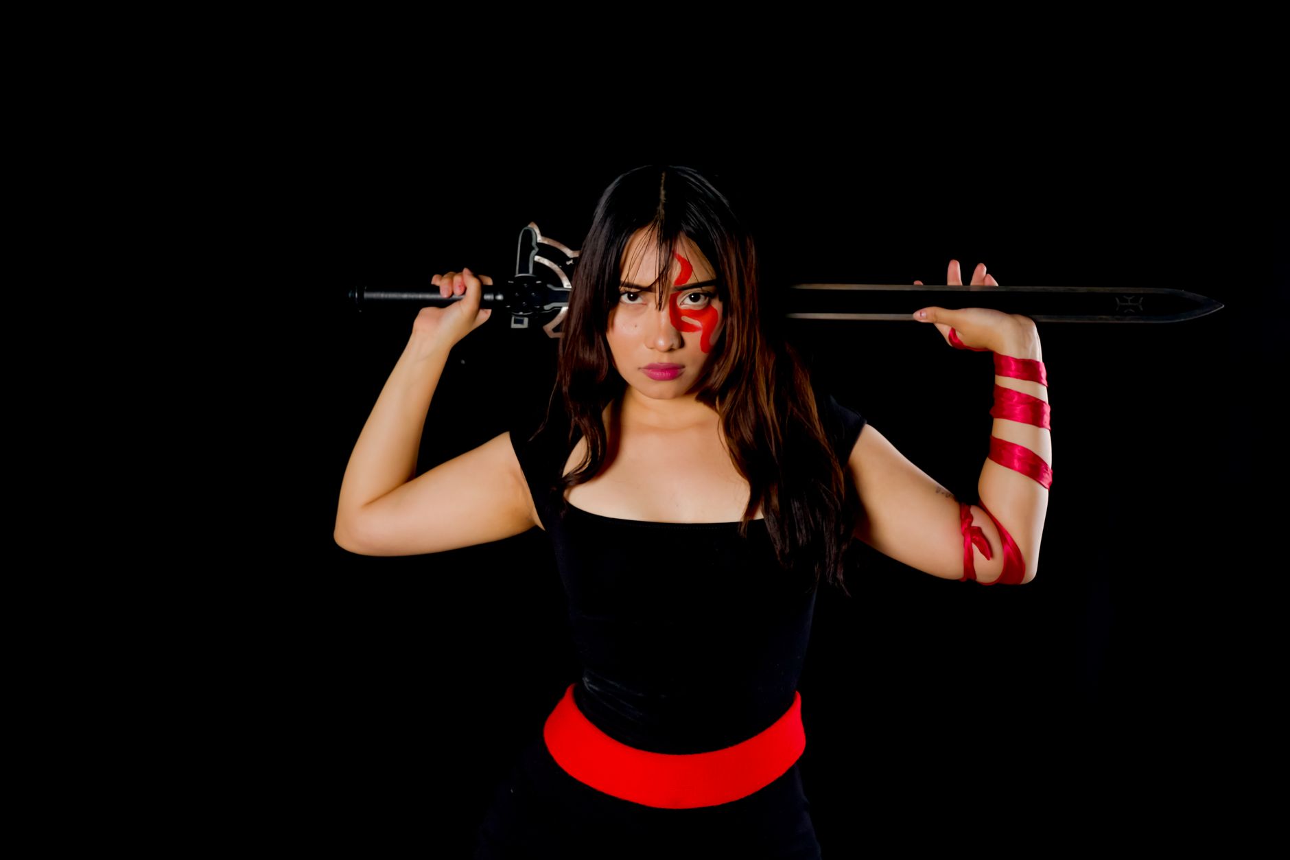 Fierce female warrior in cosplay with sword and face paint, poised against a black background.