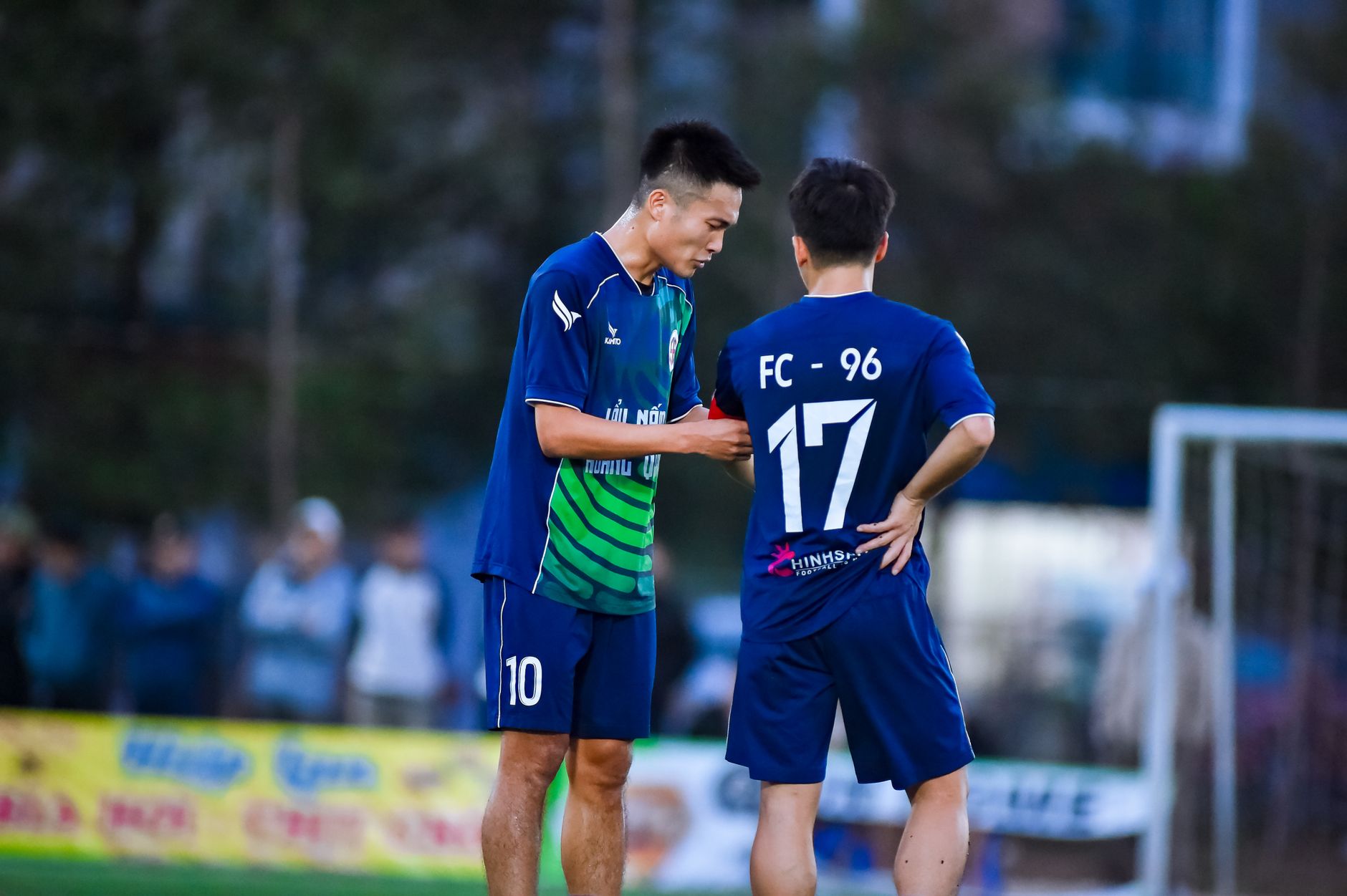 Two soccer players in blue jerseys strategize during a match in Hà Nội, Vietnam.