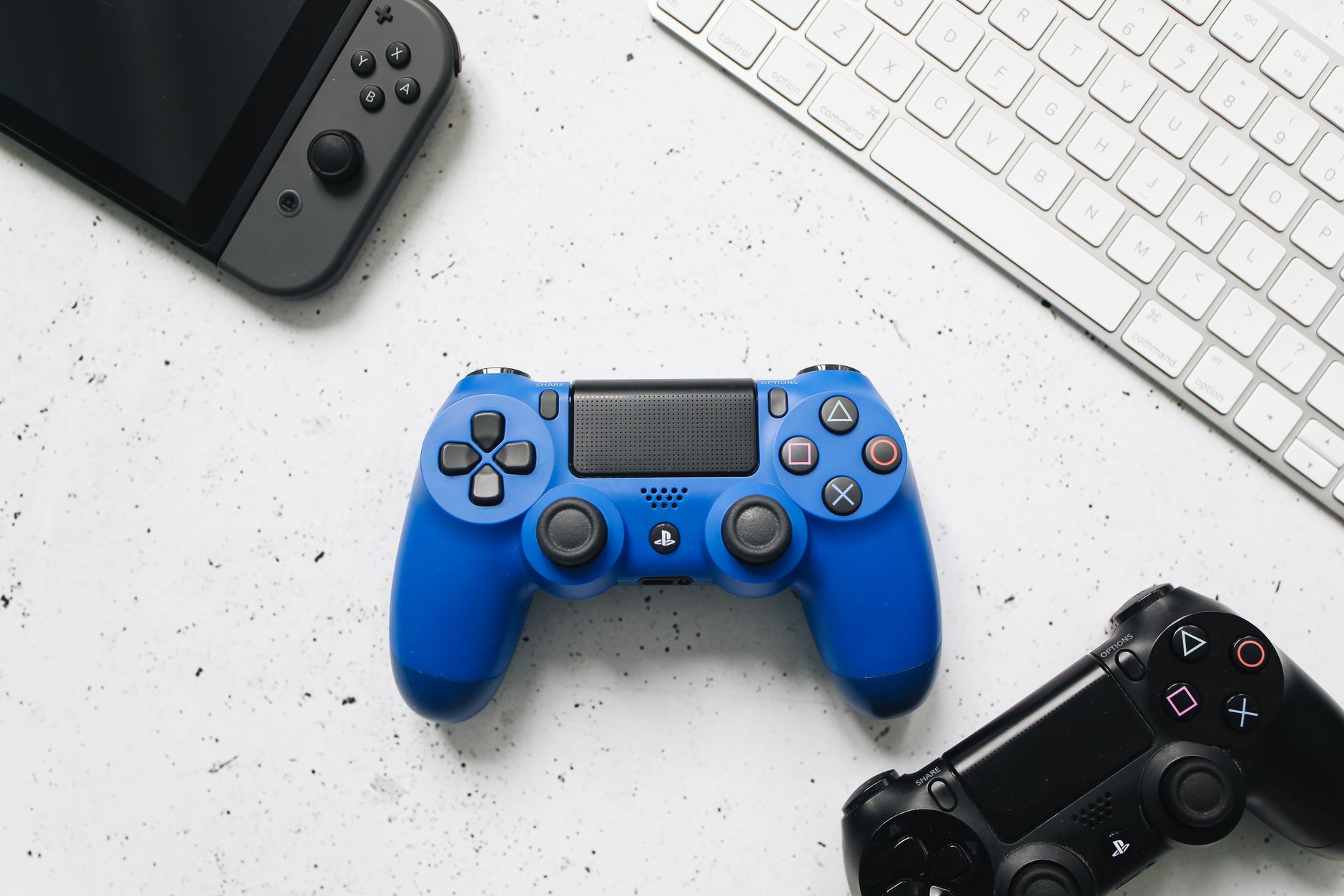 Top view of various gaming controllers and a keyboard on a white surface.