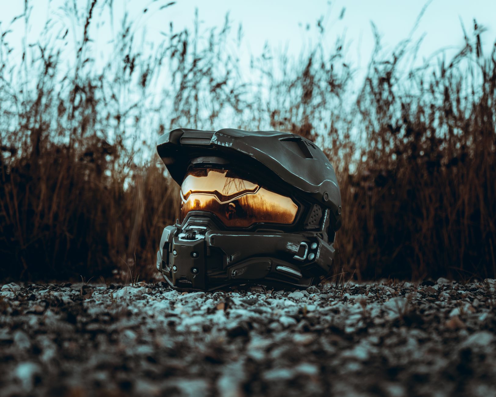 A futuristic helmet with a reflective visor placed outdoors on rocky ground, bathed in sunset light.