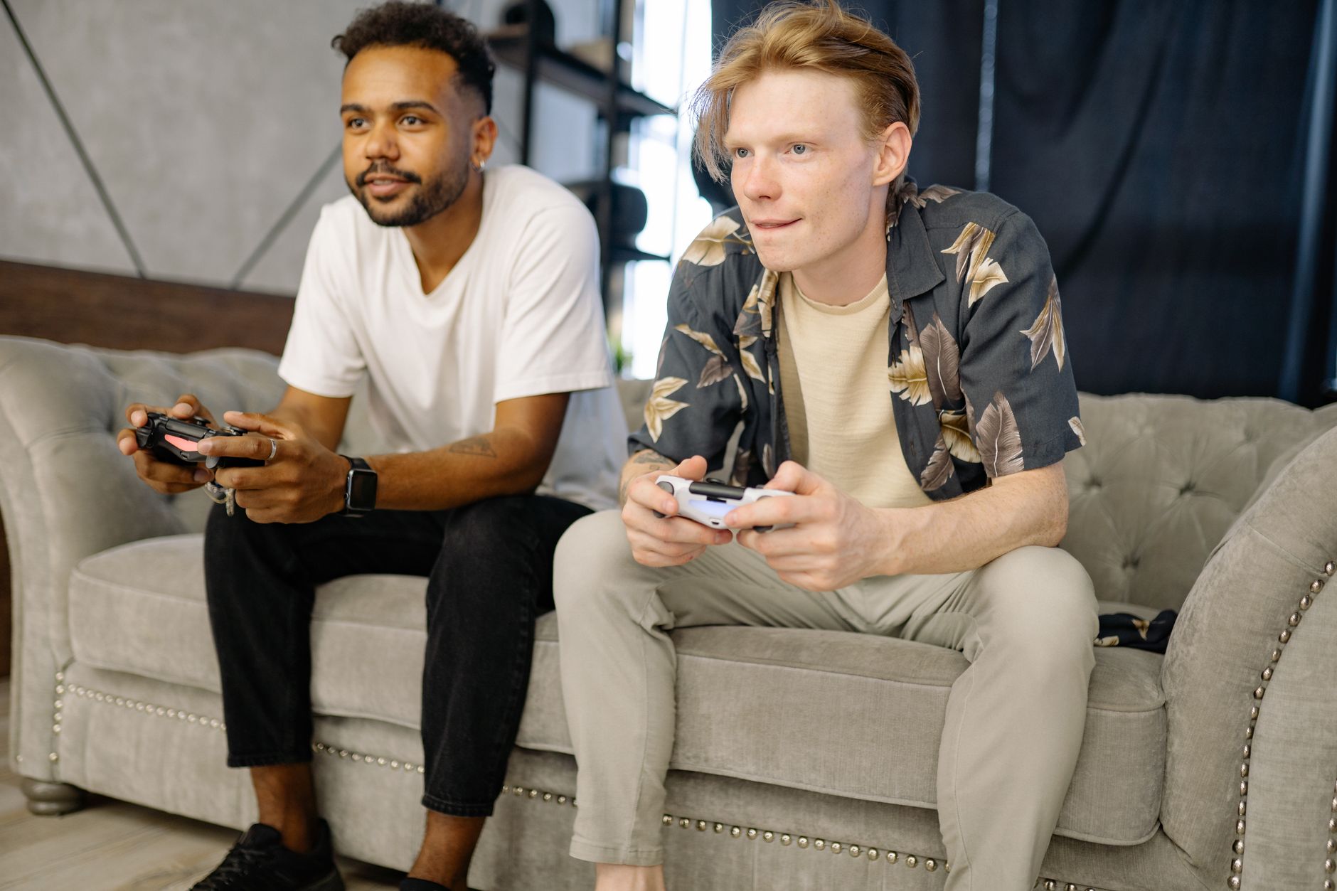 Two friends sitting on a sofa, playing video games together at home.