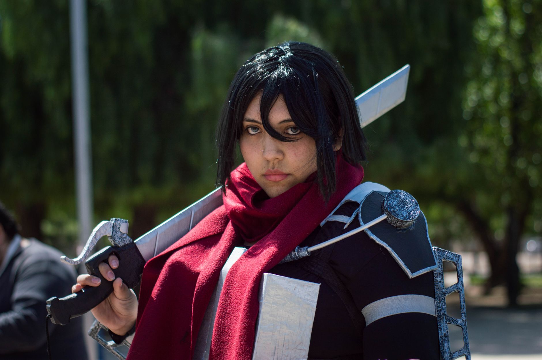 A focused cosplayer in detailed costume poses with a sword outdoors.