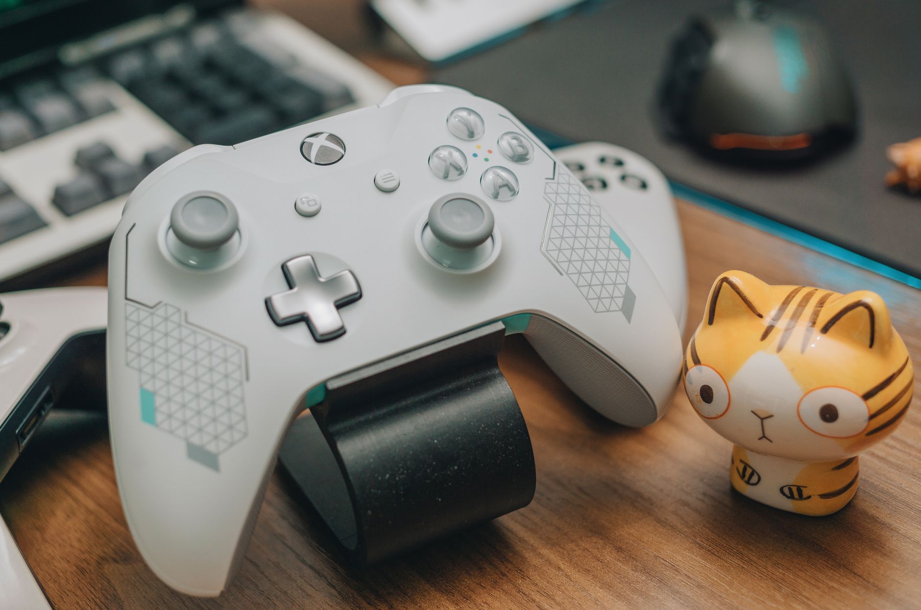 Close-up of an Xbox game controller with a toy, mouse, and keyboard on a desk, showcasing a gaming setup.