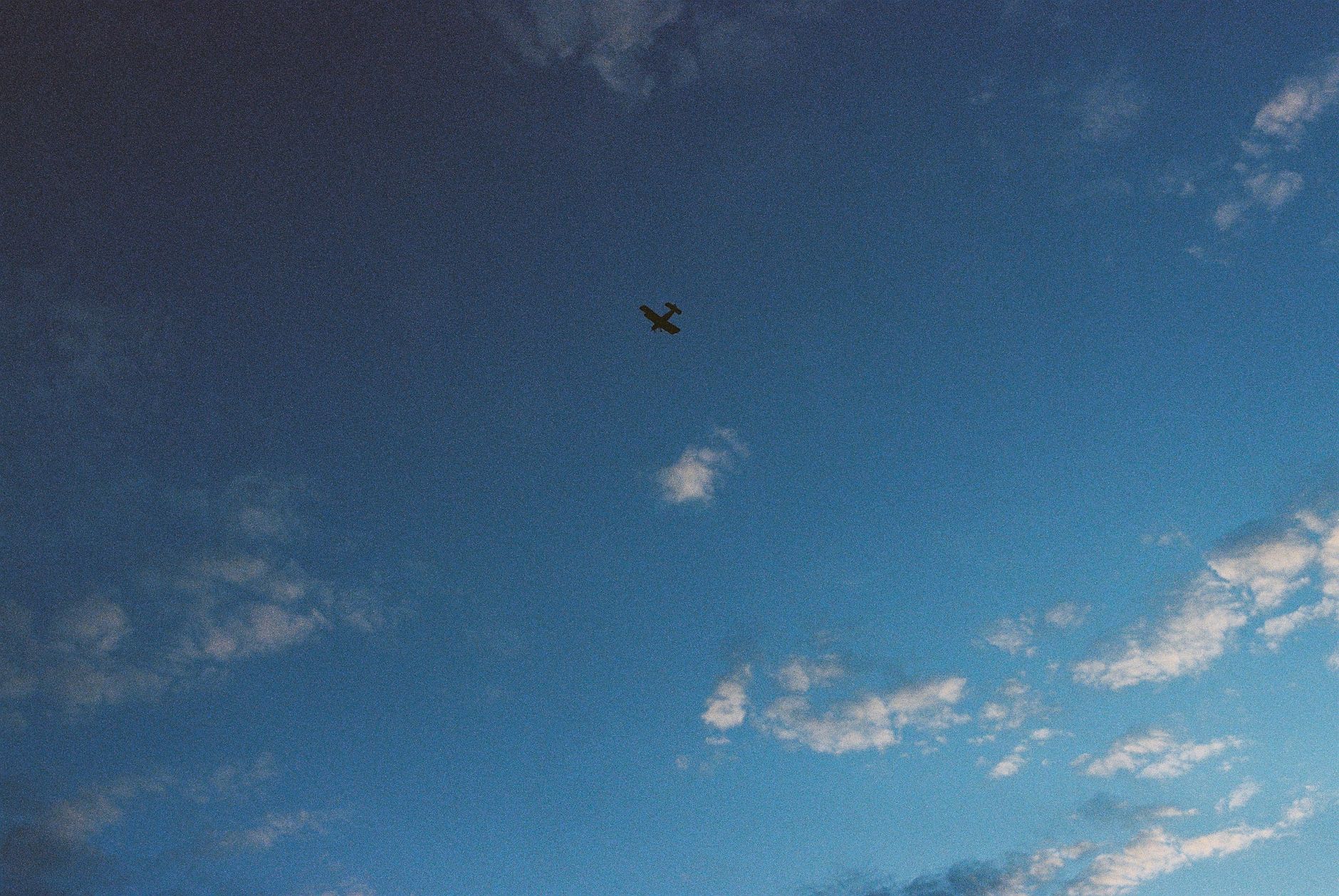A small airplane flying high among clouds in a vast, clear blue sky.