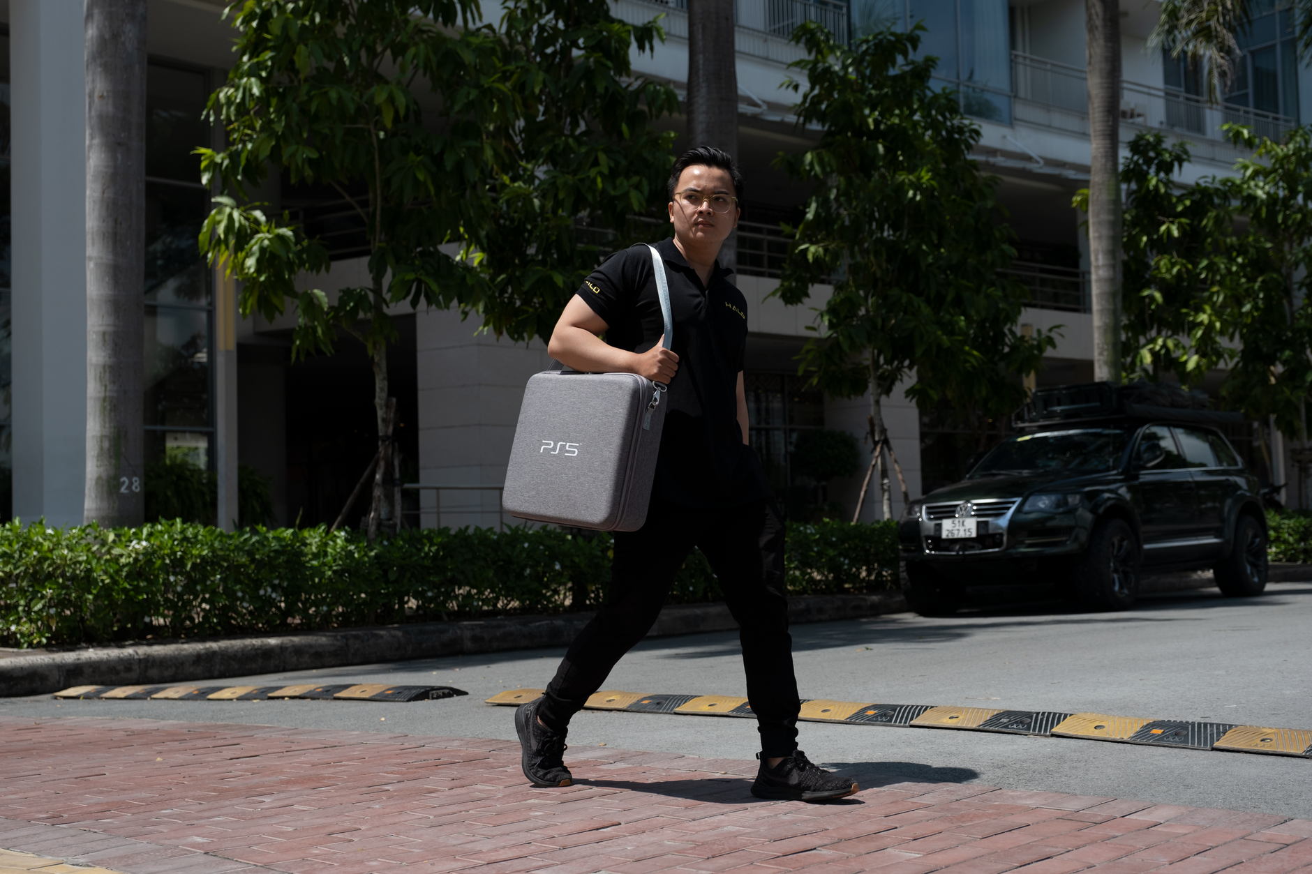 A person carrying a PS5 case walks on a city street in daylight.
