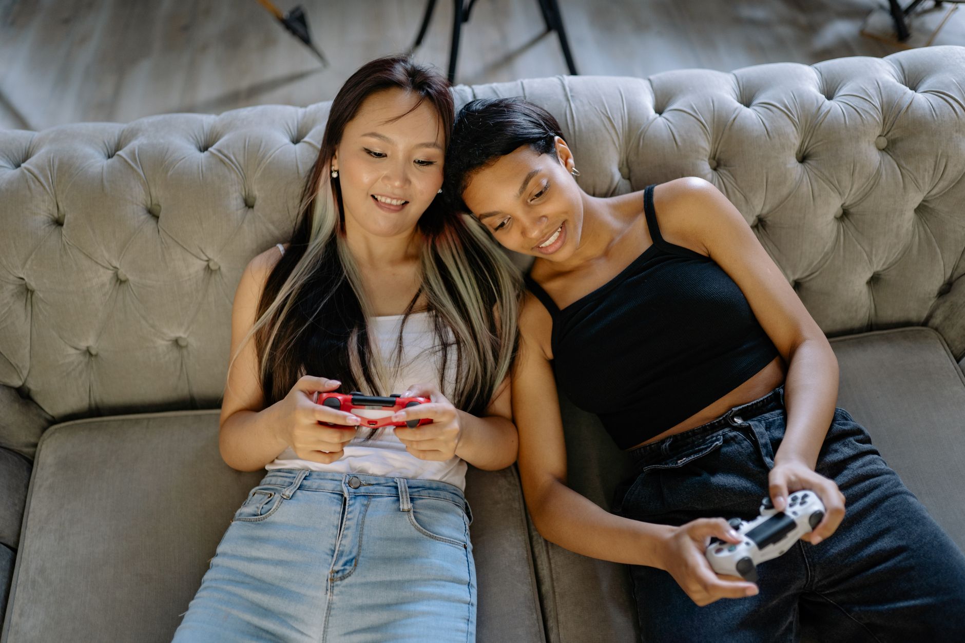 Two women relaxing and playing video games on a comfortable sofa together.