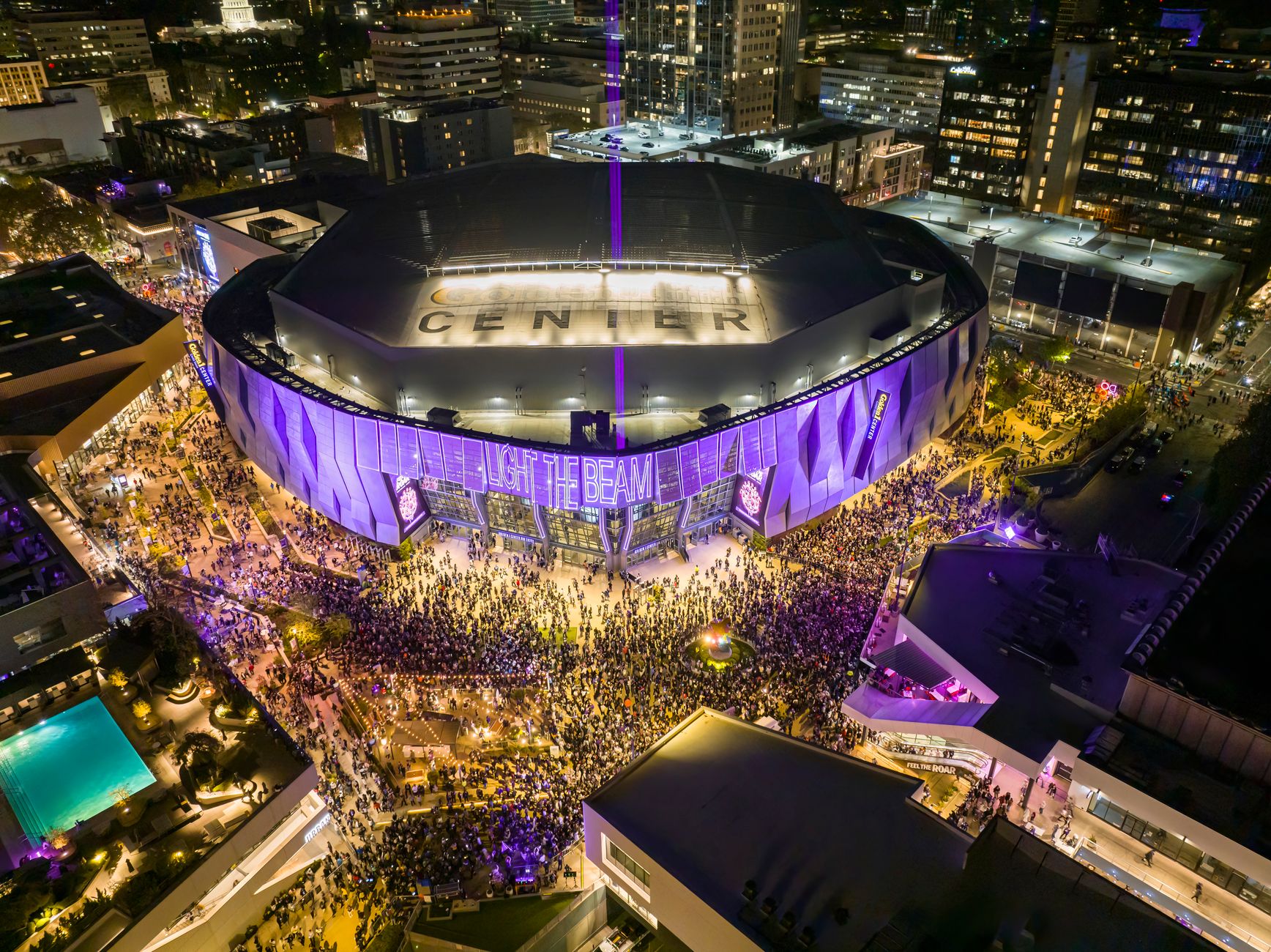 A vibrant night aerial view of Golden 1 Center in Sacramento, California during a lively event with a large crowd.