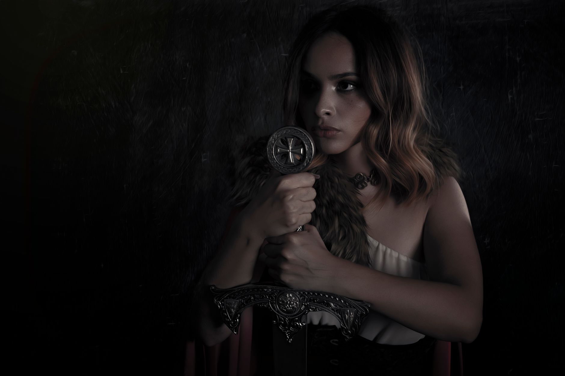 A dramatic and moody portrait of a woman dressed in a medieval warrior costume, holding a sword.