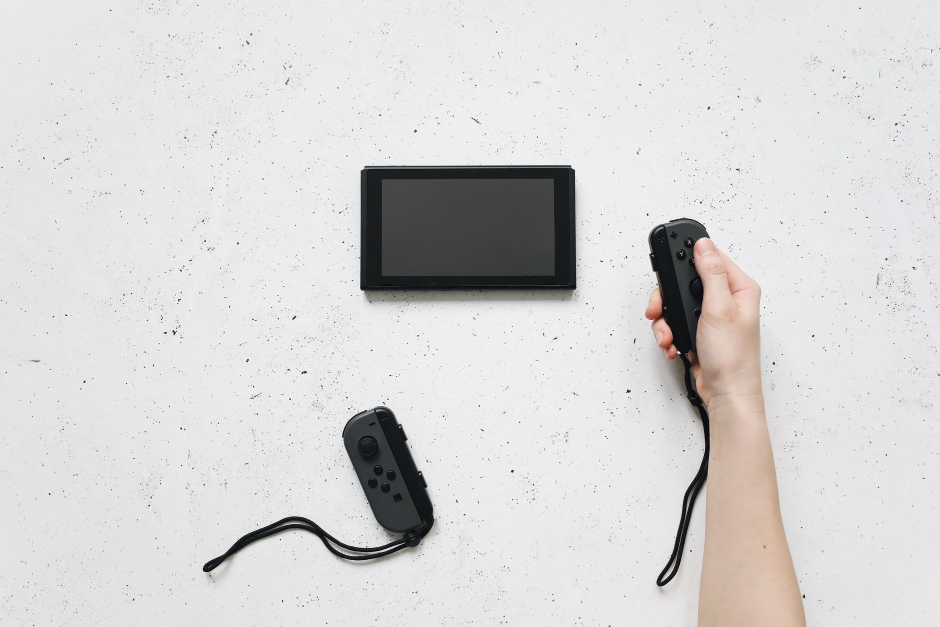 A person holds a Joy-Con controller with a Nintendo Switch on a white textured surface.