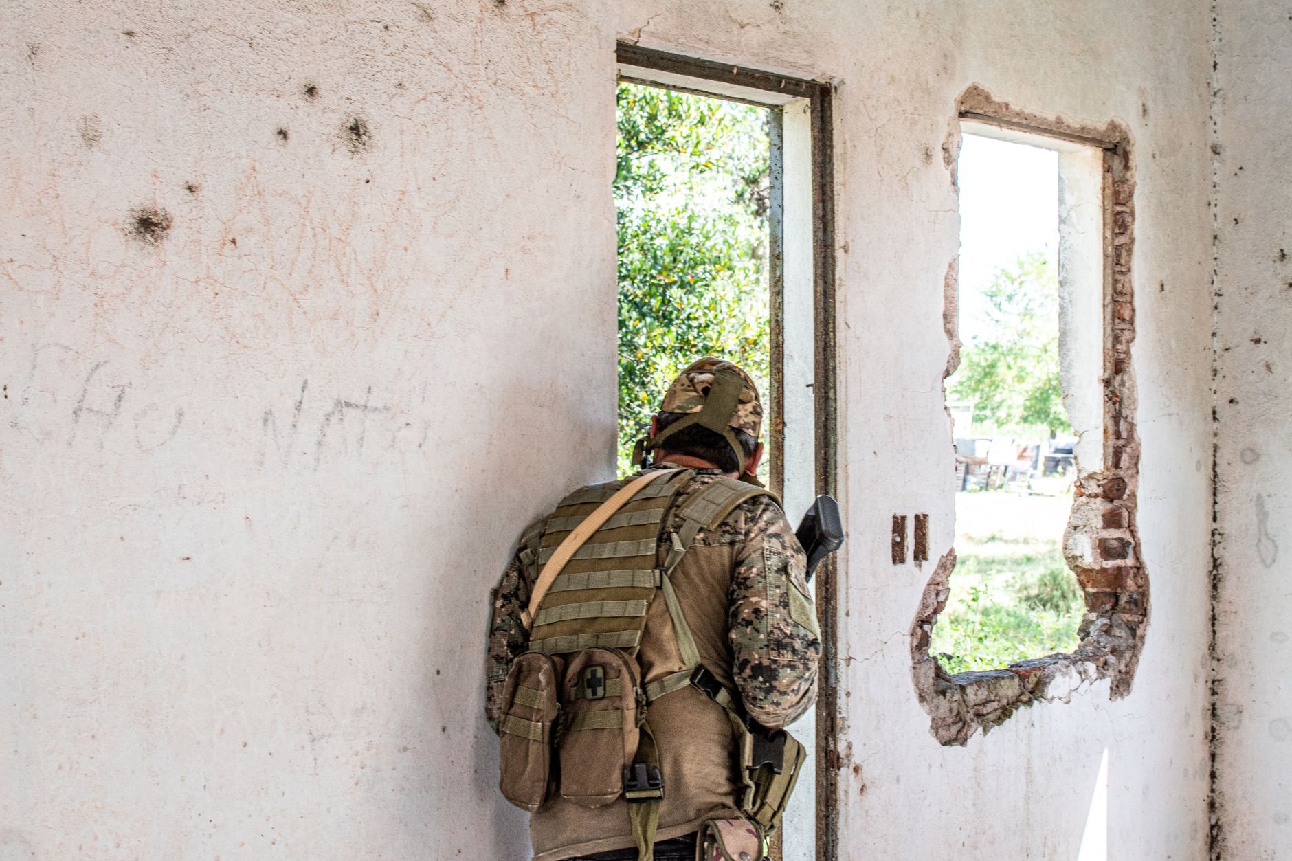 Airsoft player in camouflage navigating through a deserted, partially destroyed building.