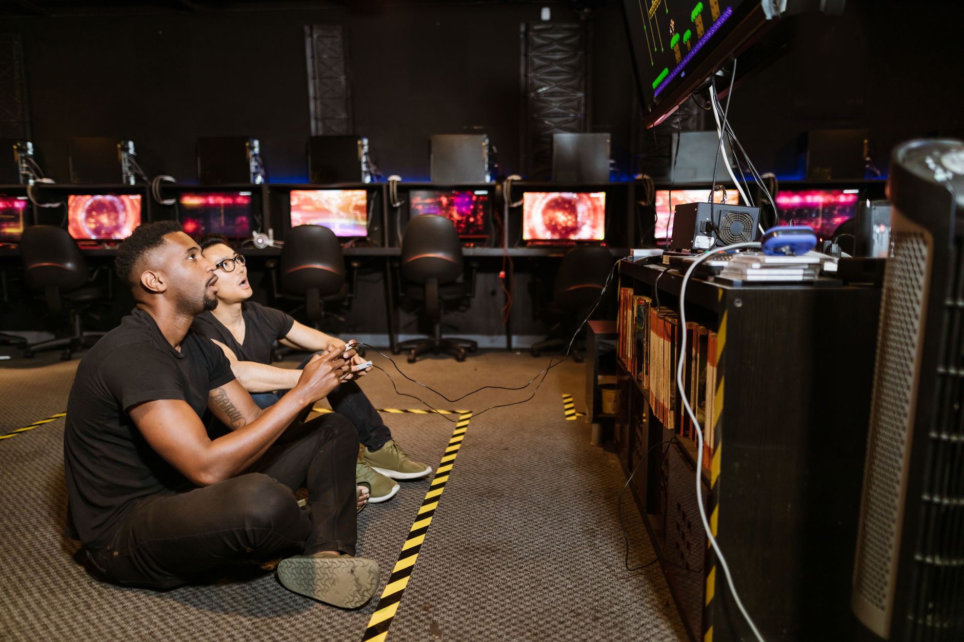 Two diverse men focused on gaming in a modern arcade setting, showcasing technology and camaraderie.