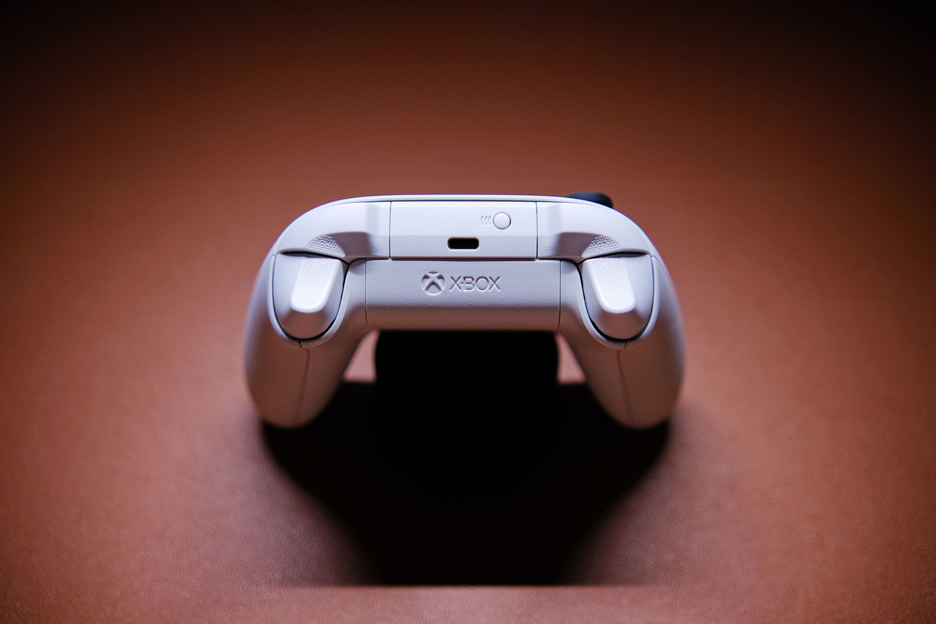 A white Xbox game controller beautifully captured on a light brown background, showcasing modern gaming technology.
