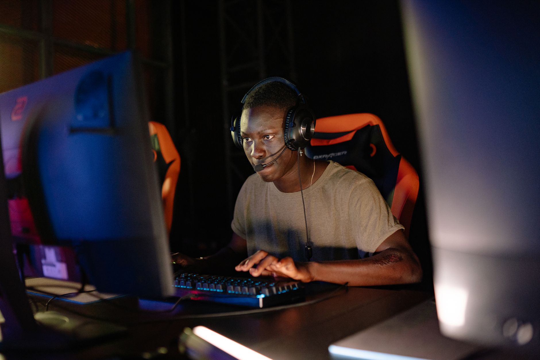 Young adult male intensely focused on computer gaming, using headset and gaming keyboard indoors.