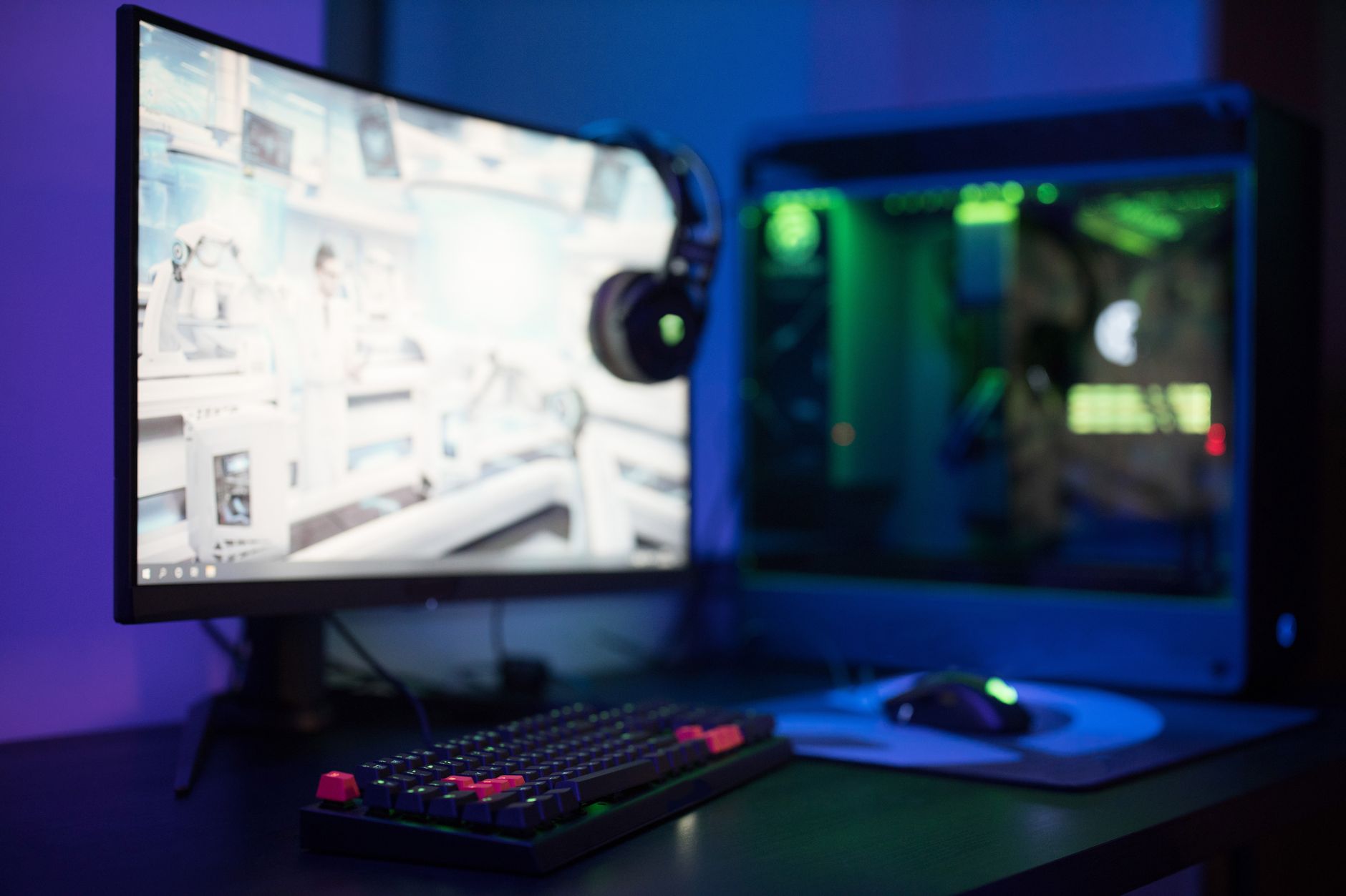 High-tech gaming setup featuring a curved monitor, RGB keyboard, and vibrant lighting.