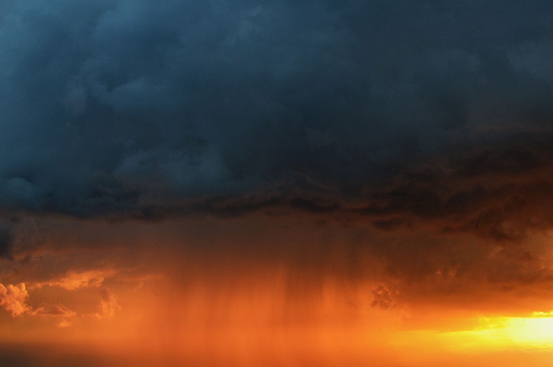 Vivid storm clouds with rain illuminated by a striking sunset sky.