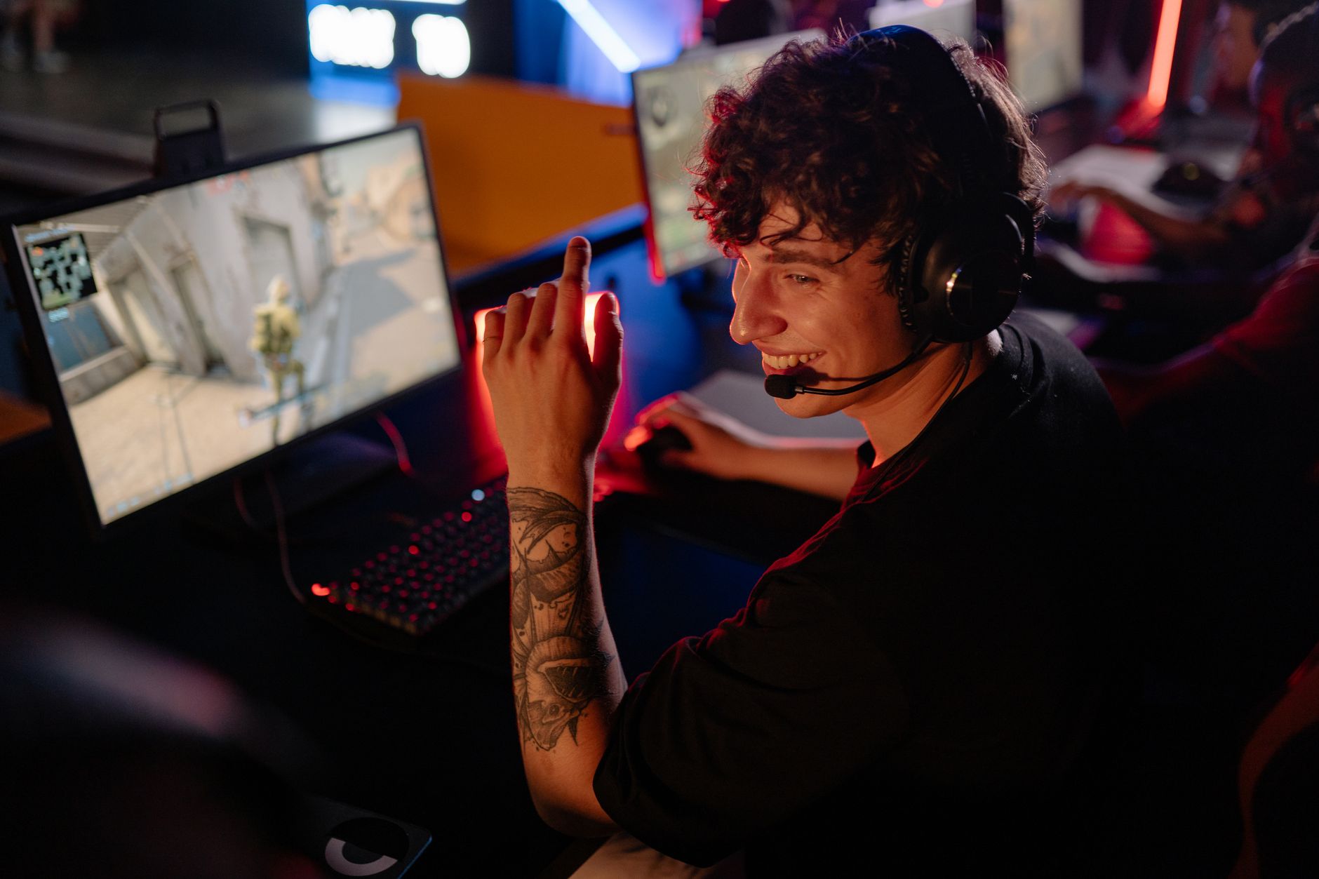 A young gamer in a black shirt enjoys an intense online game on a computer, smiling confidently.
