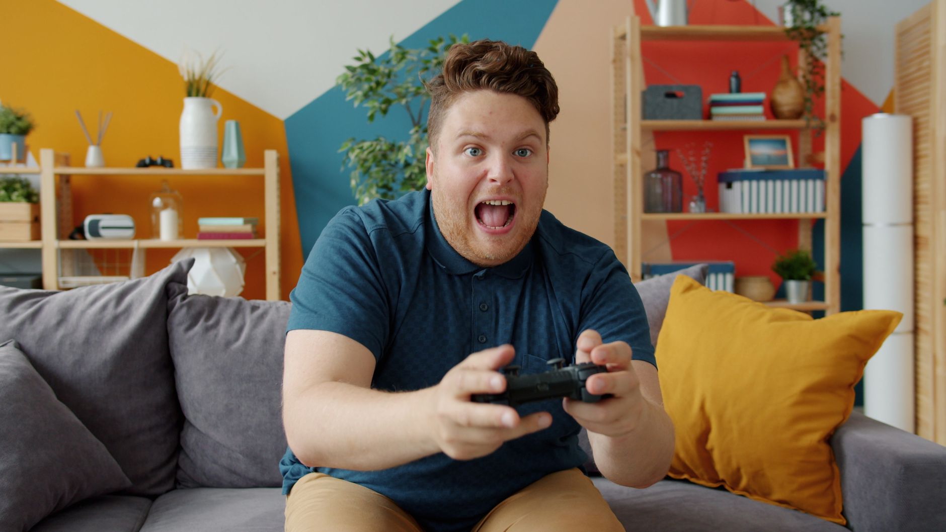 Enthusiastic adult male playing video game on console in colorful, modern living room.