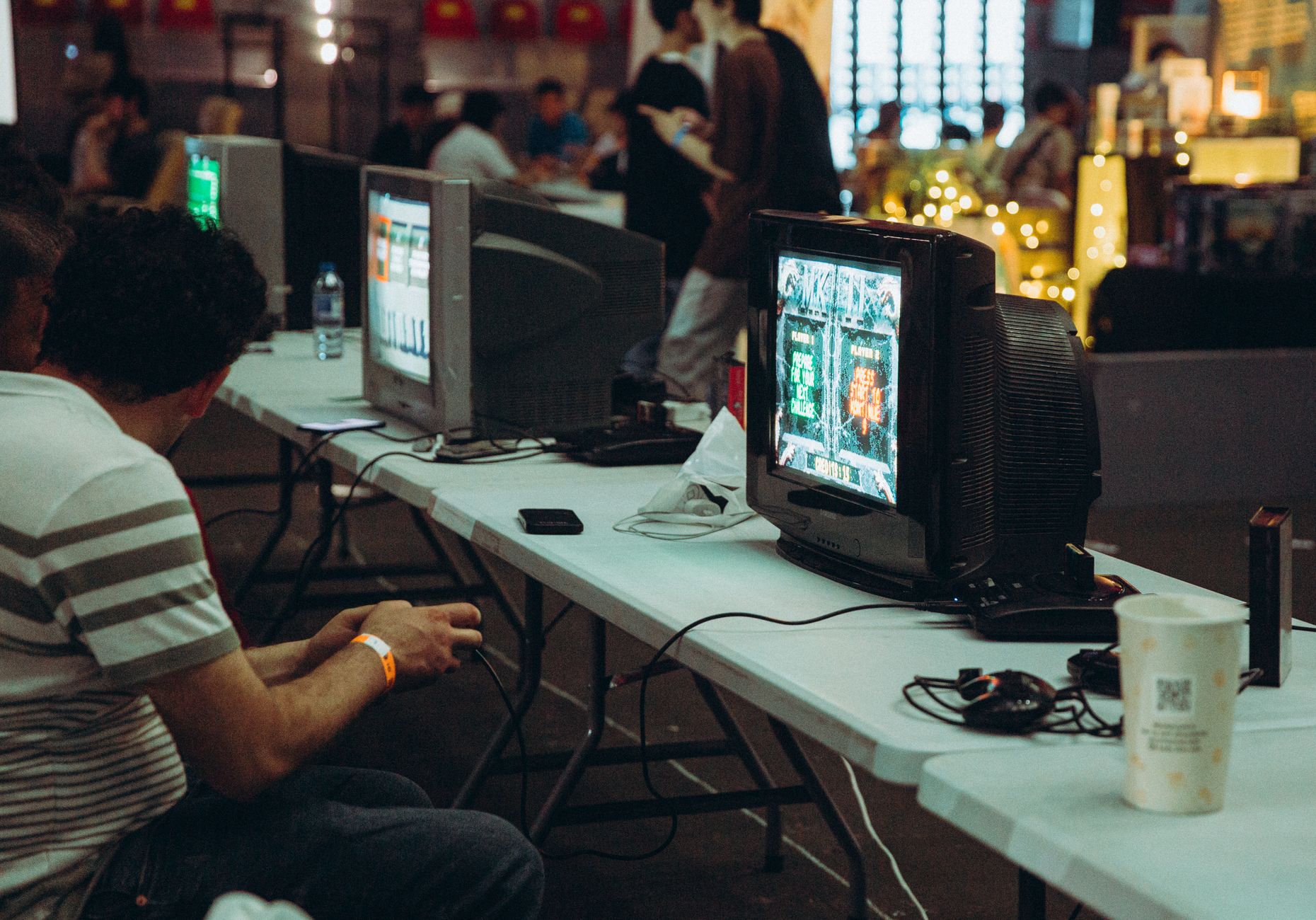 Adults enjoying a retro gaming event with CRT televisions and consoles, creating a nostalgic atmosphere indoors.
