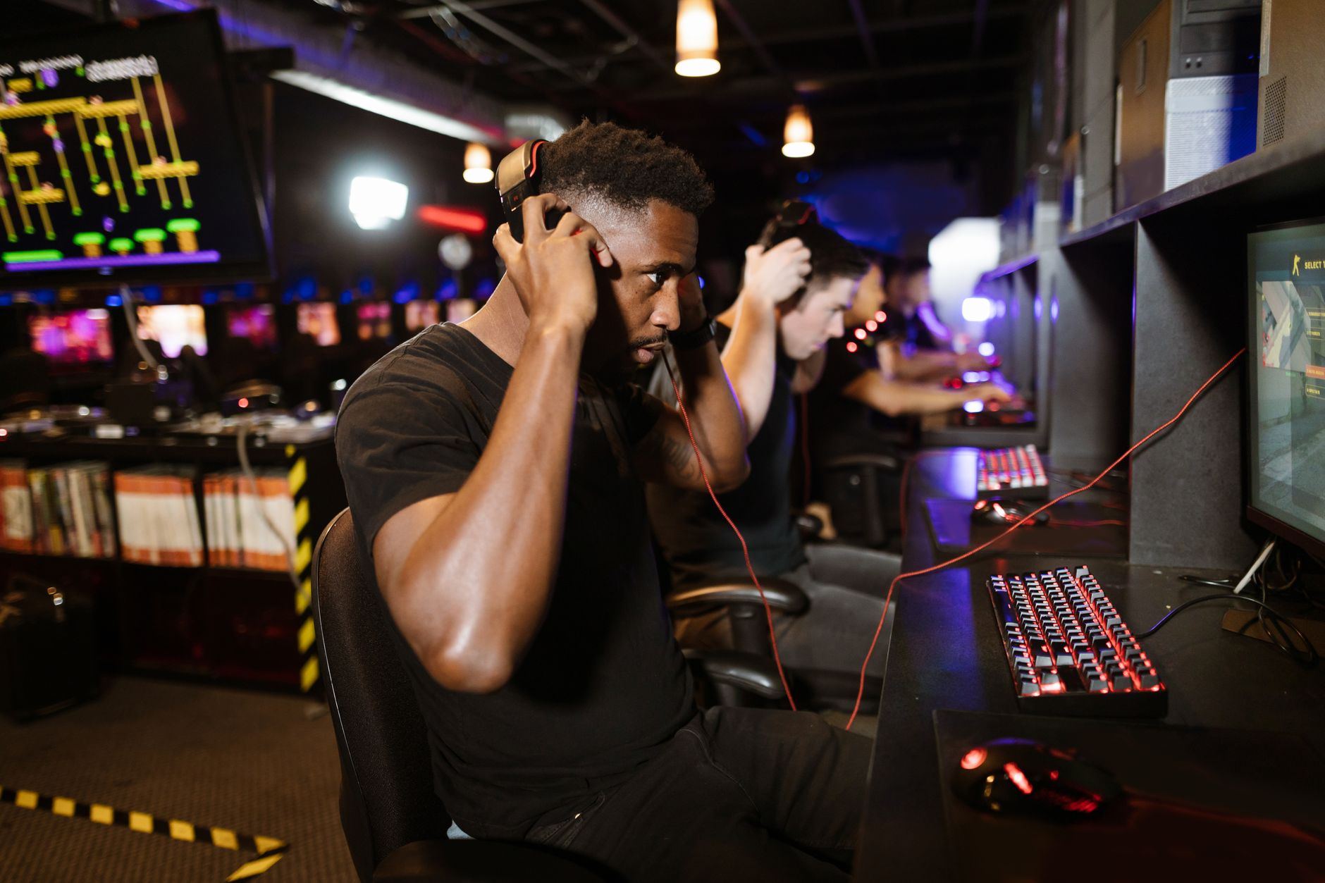 Focused gamers with headphones immersed in PC games at a lively esports venue.