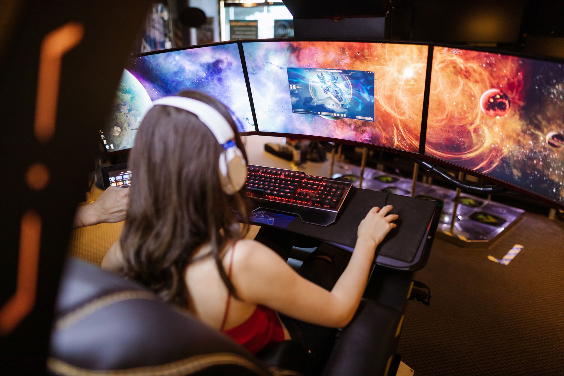 Woman with headphones playing on a multi-screen gaming setup featuring vibrant space imagery.