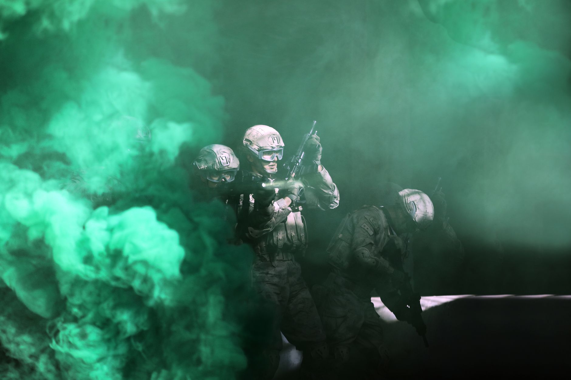 Three soldiers emerge from green smoke in a tactical military operation.