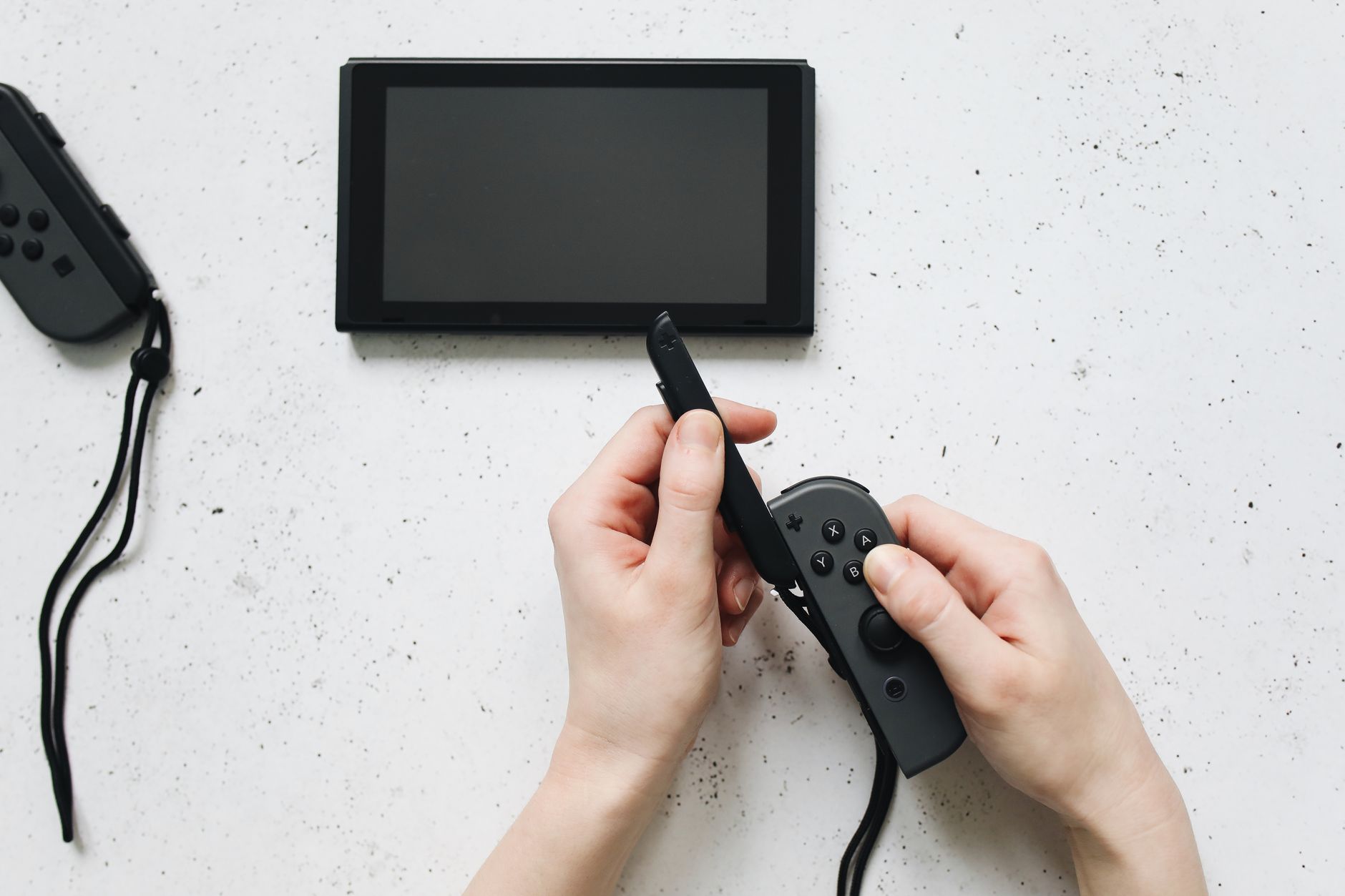 Close-up of hands holding a game controller on a white surface by a portable gaming device.