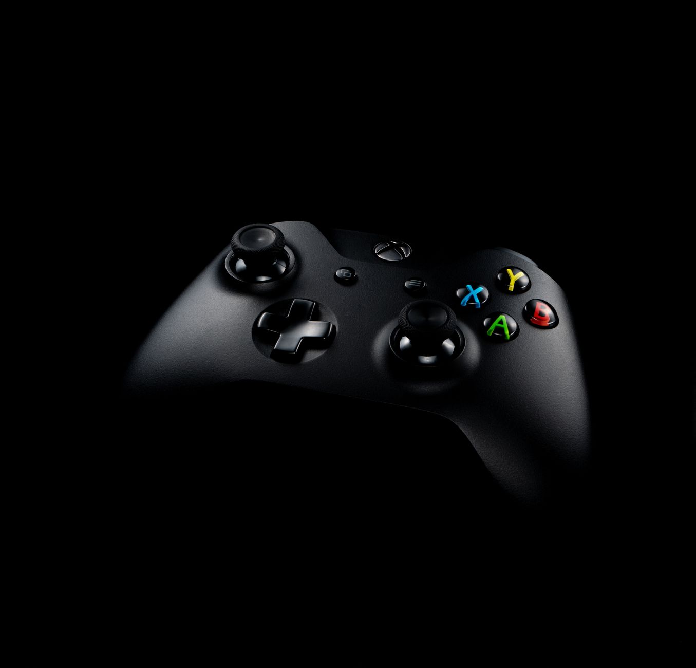 Close-up of a black wireless gaming controller on a dark background, highlighting its buttons.