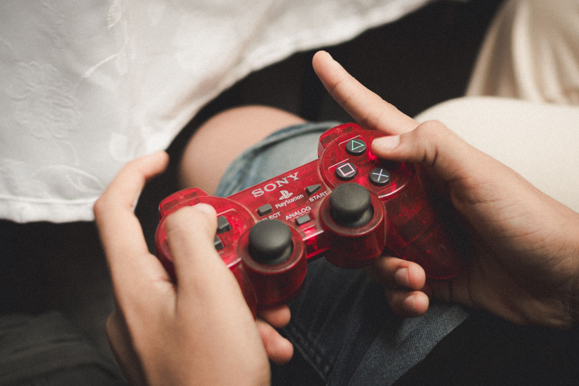 Person playing with a red PlayStation controller, evoking nostalgia for classic gaming.