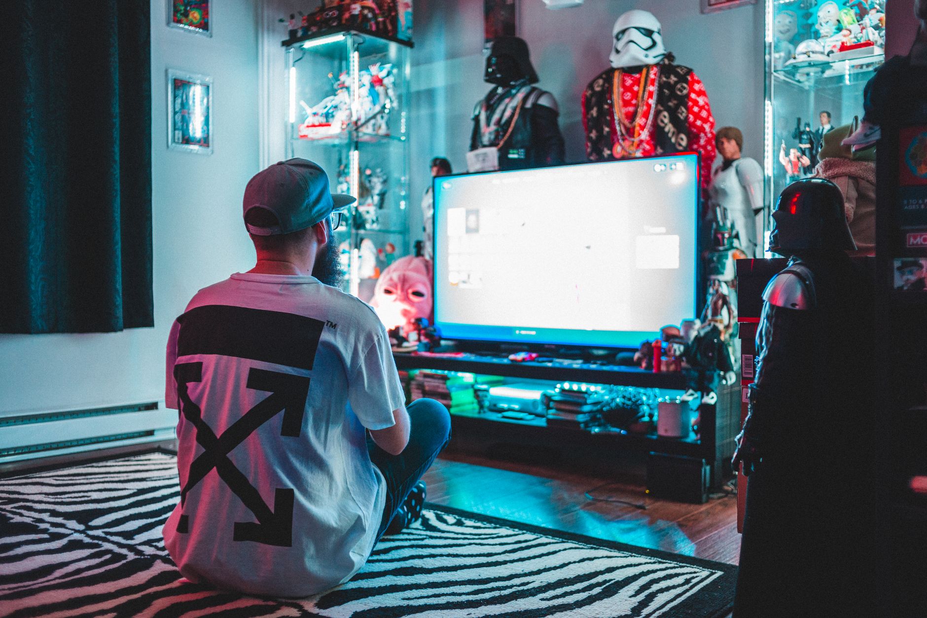Back view of anonymous male sitting on floor near modern monitor and playing video game in room with comic stuff